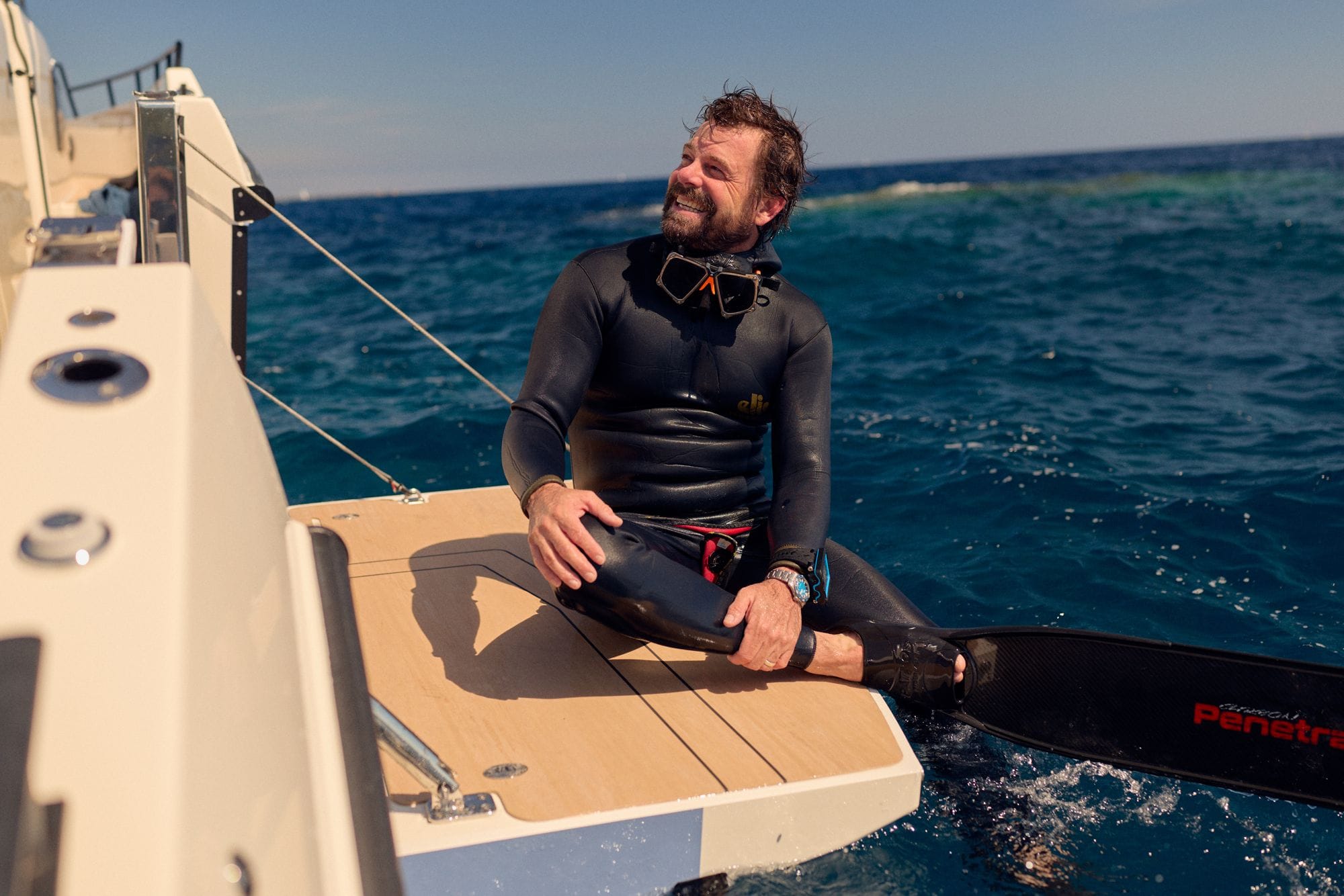 A diver in a wetsuit sitting on the C38 swim platform