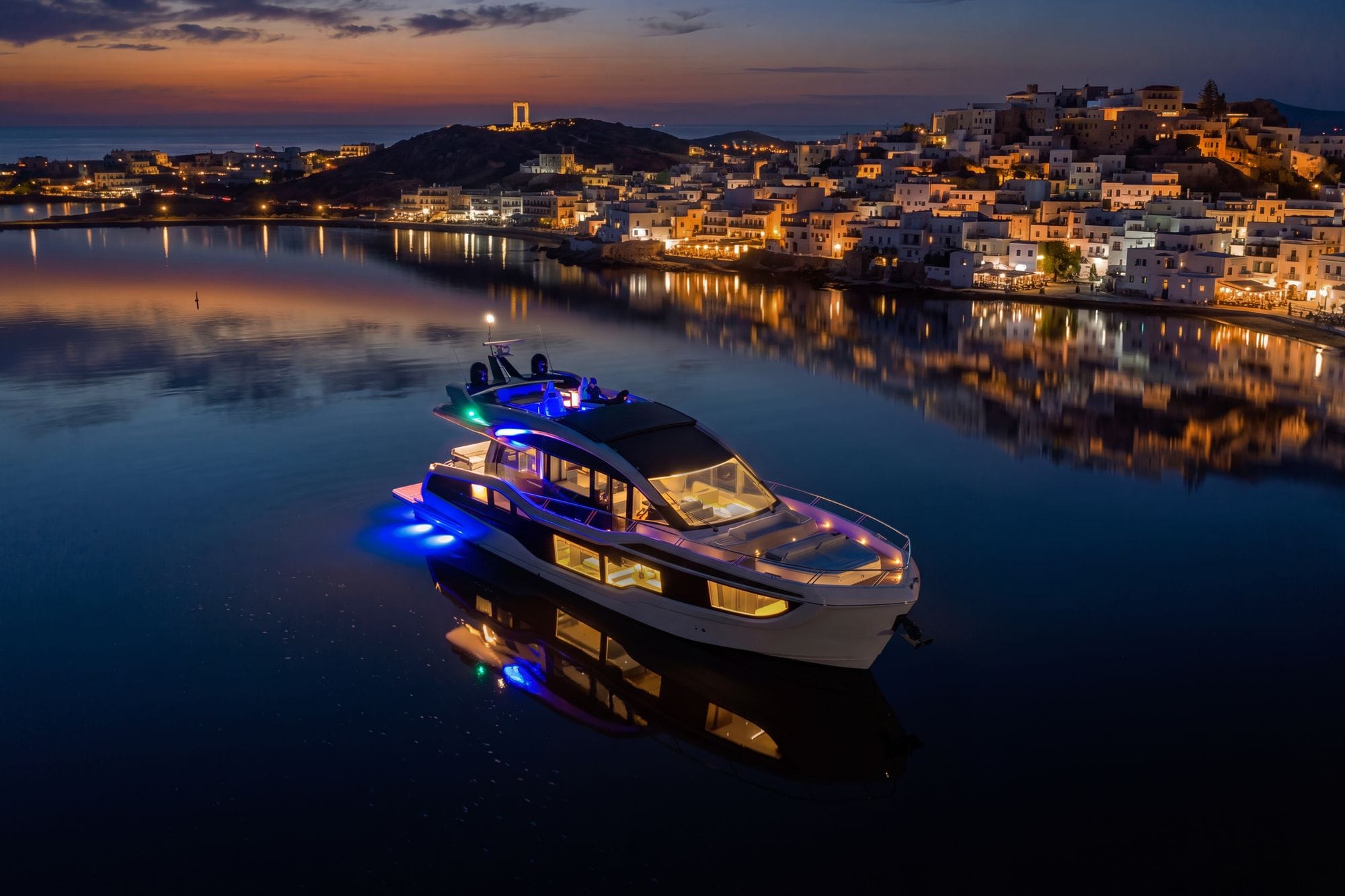 The 570 SKY lit at night off a harbour town